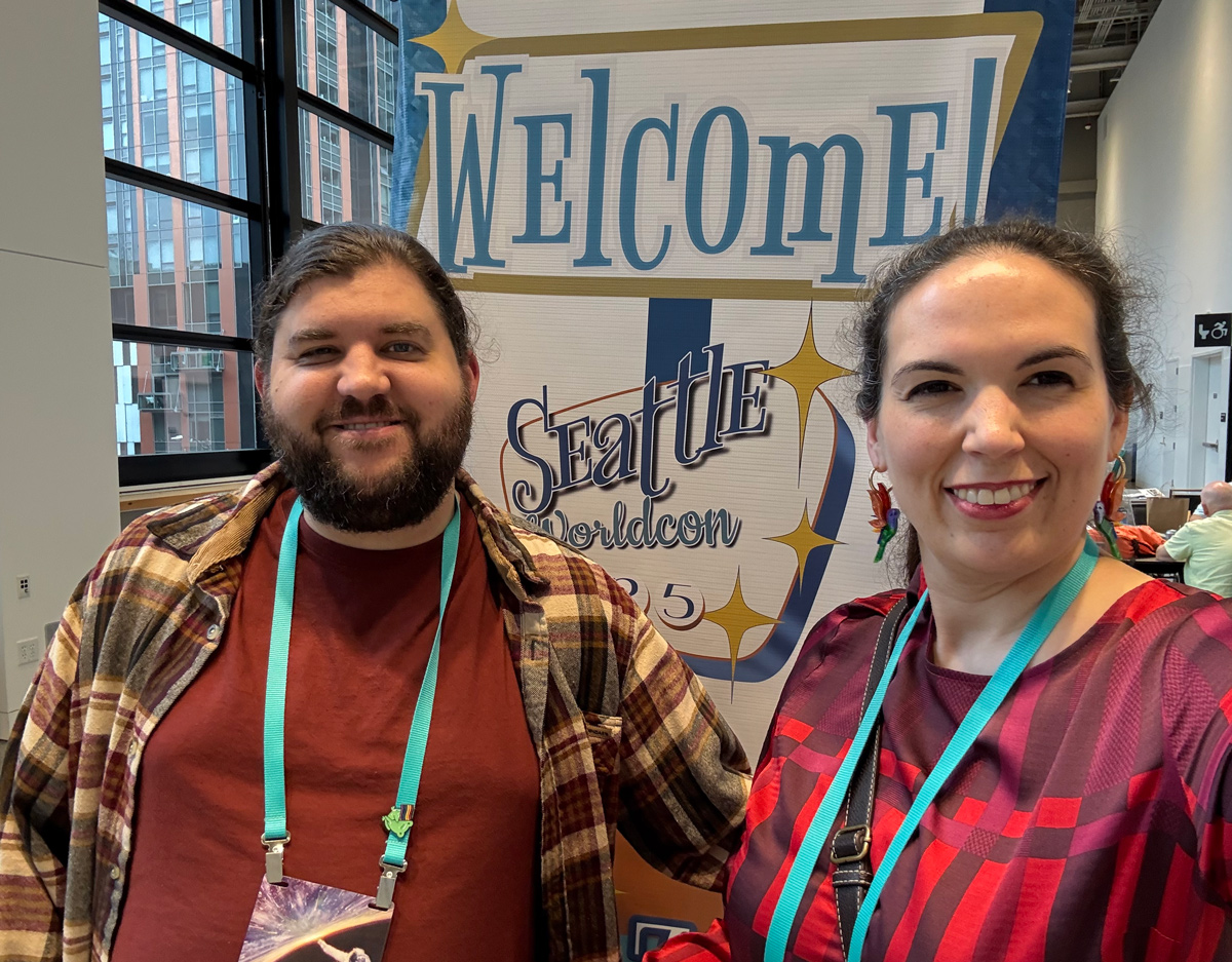 Kestrel and Alex in front of a Welcome to Worldcon Sign